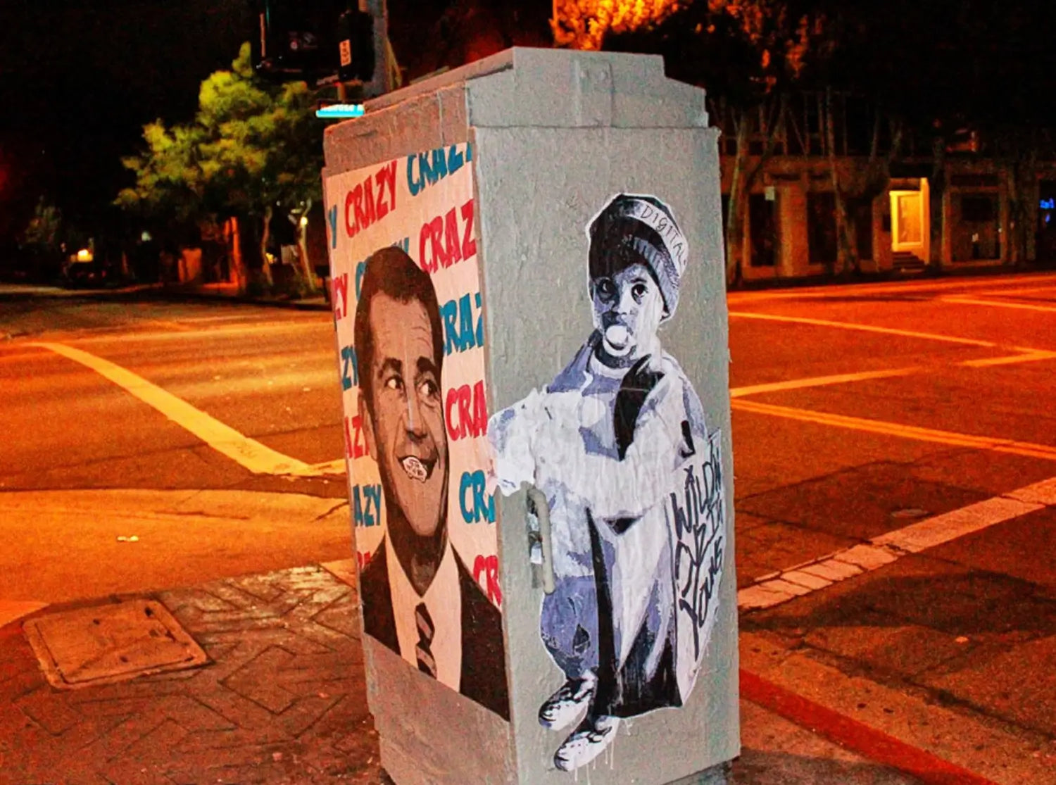 Street art on a utility box with a person and text in an urban setting at night.